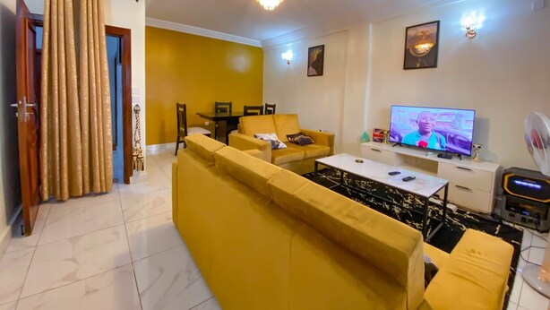 Un salon avec un canapé jaune, un téléviseur et un lustre.
