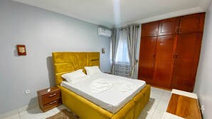 Une chambre avec un lit jaune, une armoire en bois, une petite table de chevet en bois et un tapis moelleux.