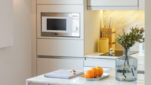 Une cuisine moderne dotée d’un four à micro-ondes encastré, d’un petit îlot central agrémenté d’un vase et d’oranges, et de deux tabourets de bar noirs.