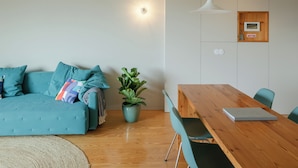 A modern living room with a teal sofa, a wooden dining table, and a potted plant. - Penthouse with Private Balcony | Baumhaus Serviced Apartments | Central Porto (Porto)