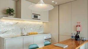 A modern kitchen with a marble countertop, a built-in oven, a microwave, and a wooden dining table with chairs. - Penthouse with Private Balcony | Baumhaus Serviced Apartments | Central Porto (Porto)