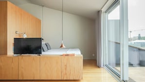 A modern bedroom with a wooden bed, a TV, and a desk. - Penthouse with Private Balcony | Baumhaus Serviced Apartments | Central Porto (Porto)