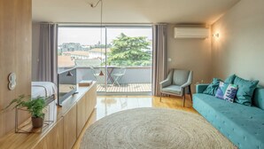 A modern living room with a sofa, a dining table, and a balcony with a view of the city. - Penthouse with Private Balcony | Baumhaus Serviced Apartments | Central Porto (Porto)