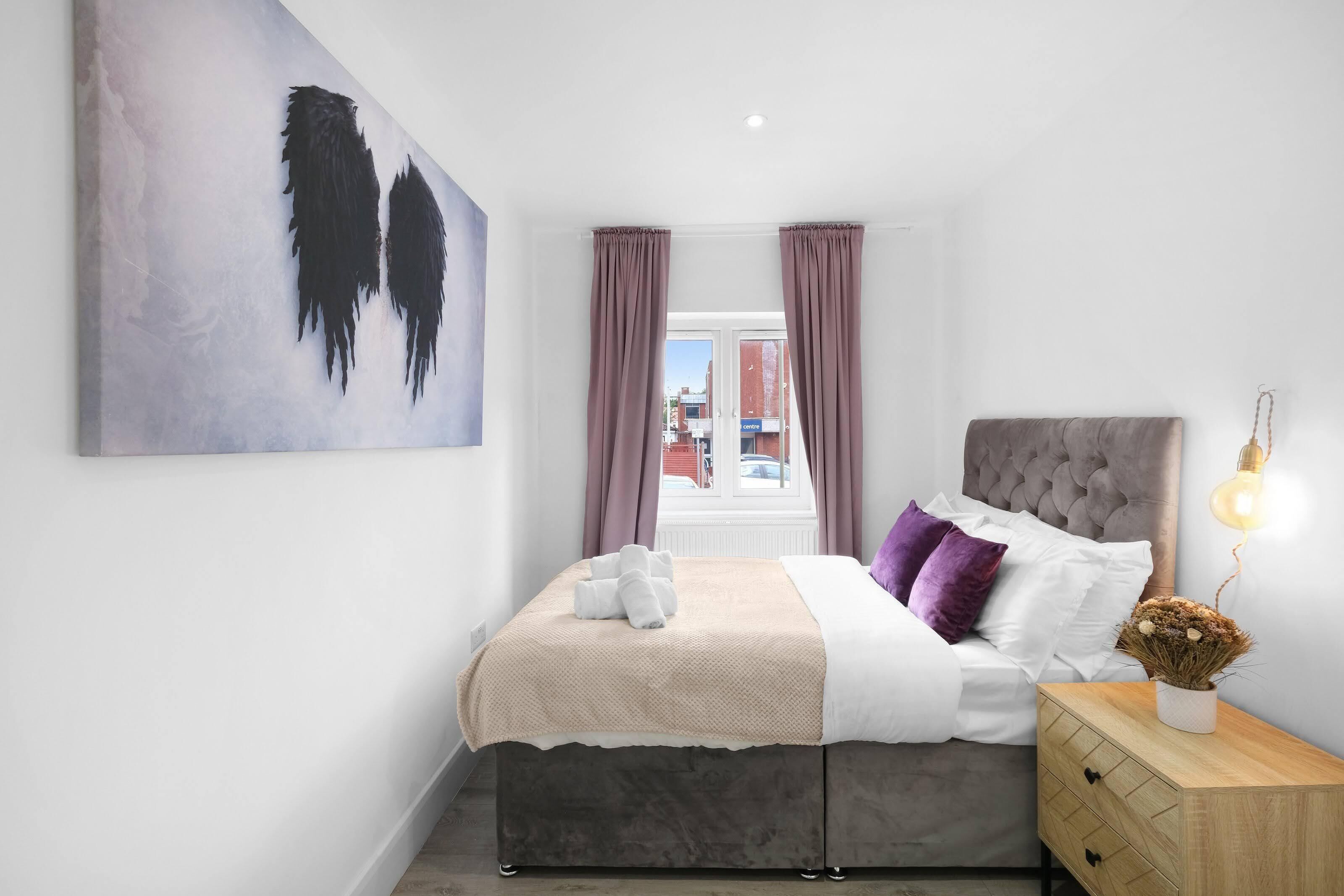 A bedroom with a bed, a nightstand, a lamp, and a window with curtains.