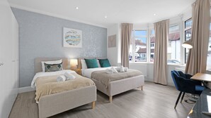 A modern hotel room with two beds, a dining area, and large windows with curtains. - Modern 3 Bedroom, 2 Bathroom Home in Edgware (Edgware)
