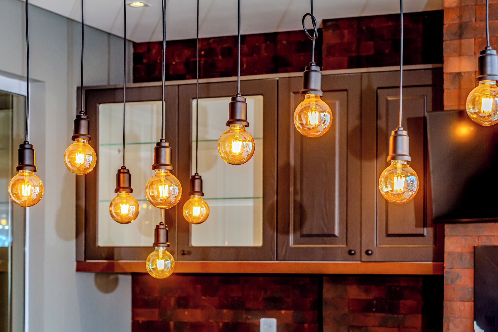 A kitchen with hanging Edison bulbs, wooden cabinets, and a brick backsplash.