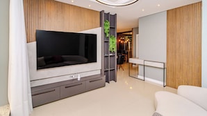 Een moderne woonkamer met een grote flatscreen-tv, een grijze entertainmentkast, een witte bank en een houten accentmuur.
