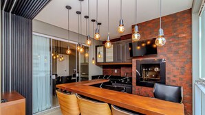 Een moderne keuken met een houten kookeiland, hangende pendantlampen en een accentmuur van baksteen.