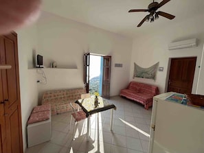 Una habitación con ventilador de techo, sofá, mesa con un florero, cama y puerta.