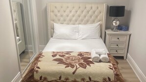 A neatly made bed with a floral bedspread, a bedside lamp, and a nightstand with a tissue box. - Spacious Basement Apartment in Rouge Hill Near Highway 401 (Toronto)