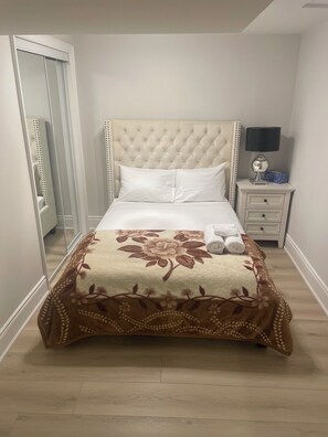 Un lit bien fait, recouvert d’une couvre-lit à motifs floraux, une lampe de chevet et une table de chevet avec une boîte de mouchoirs.