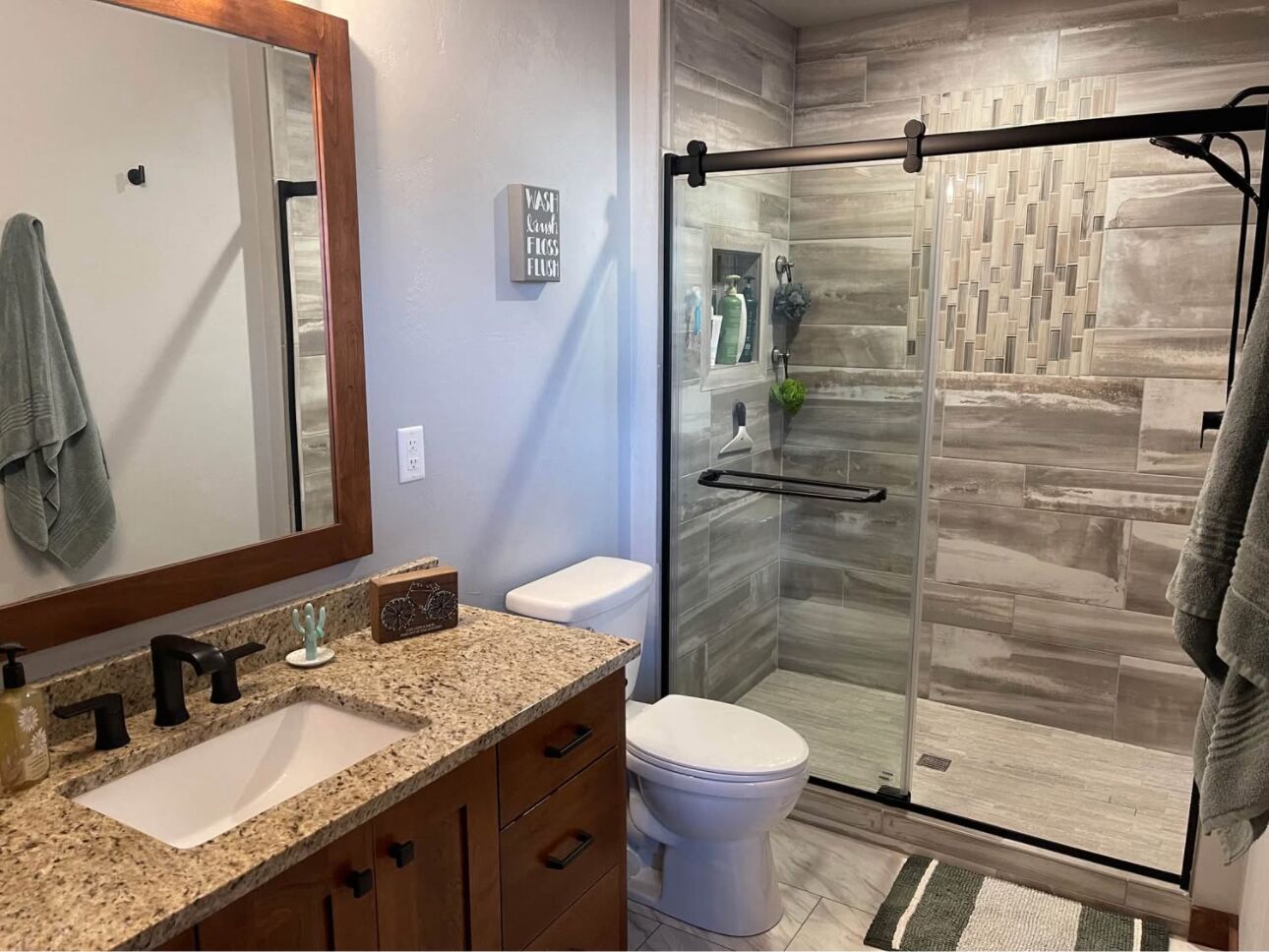 A modern bathroom with a granite countertop sink, a toilet, and a glass shower enclosure.