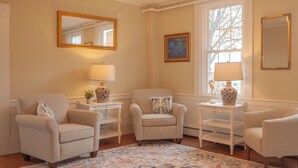 A room with two armchairs, a small table with a lamp, a painting on the wall, and a window with a view.