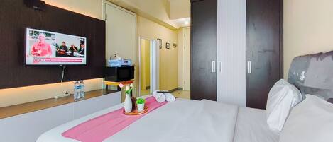 A hotel room with a bed, a TV displaying a news broadcast, a minibar, and a mirror.