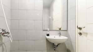 A bathroom with white tiles, a sink, a mirror, and a door. - Minimalist Studio (No Kitchen) At Anderson Supermall Mansion Apartment (Surabaya)