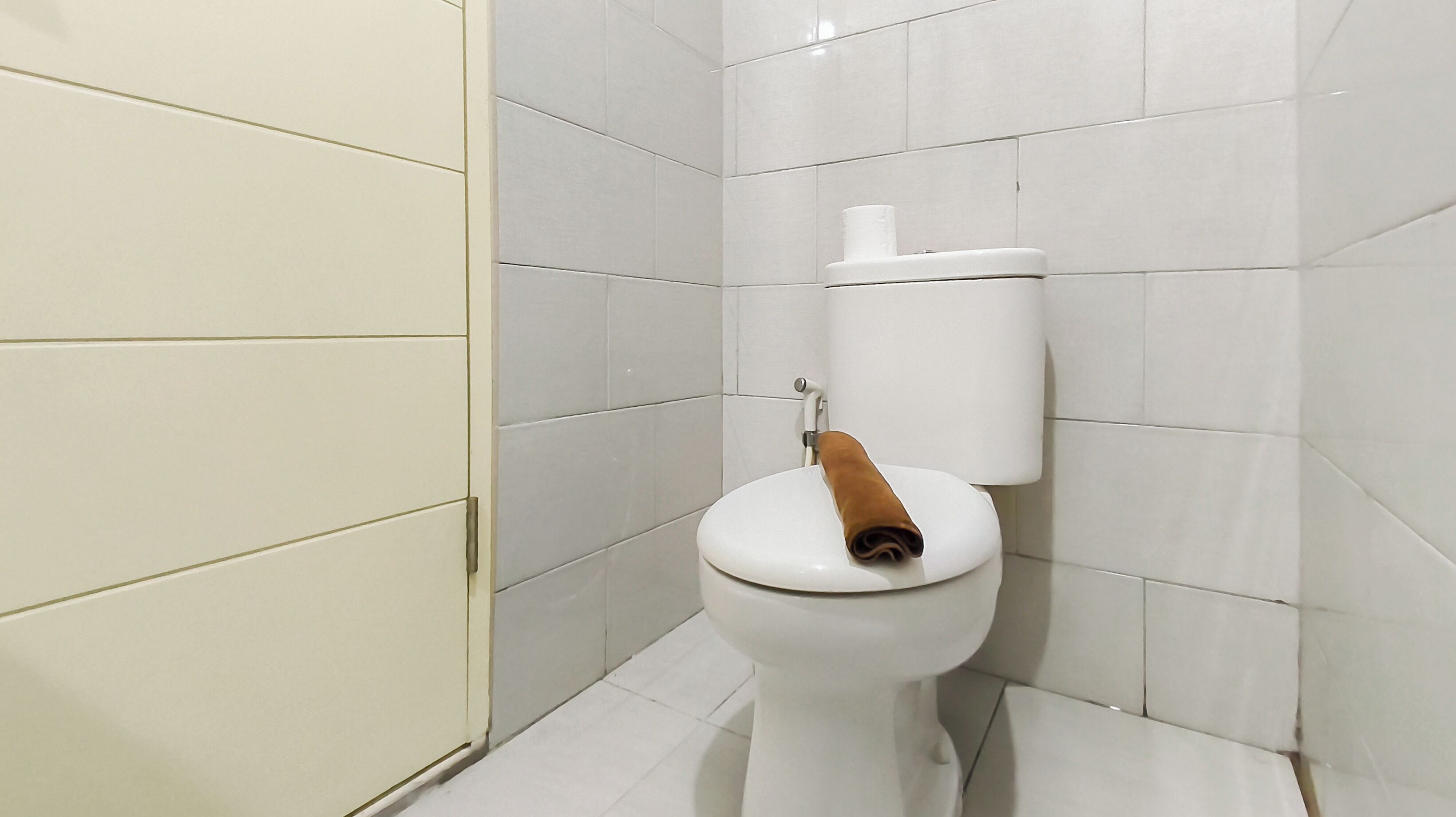 Eine weiße Toilette mit einem braunen Toilettenpapierhalter in einem Badezimmer mit weißen Fliesen.