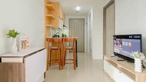 A modern kitchen with wooden chairs, a dining table, and a TV on a wooden stand. - Contemporary And Restful 2Br At Apartment Anwa Residence (South Tangerang)