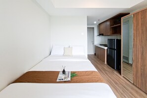 Une chambre d’hôtel moderne, équipée d’un lit, d’une table de chevet en bois, d’un magazine, d’un réfrigérateur noir et d’une armoire en bois.