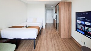A hotel room with a bed, a TV mounted on the wall, and a wooden floor. - Homey And Minimalist Studio Apartment At Anwa Residence (South Tangerang)