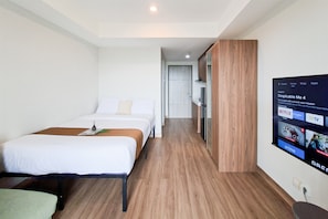A hotel room with a bed, a TV mounted on the wall, and a wooden floor. - Homey And Minimalist Studio Apartment At Anwa Residence (South Tangerang)