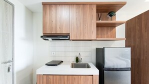 A compact kitchen with wooden cabinets, a white countertop, a stainless steel sink, and a refrigerator. - Homey And Minimalist Studio Apartment At Anwa Residence (South Tangerang)