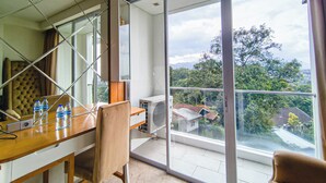 A modern room with a dining table, chairs, a sofa, and a large sliding glass door leading to a balcony with a view of greenery and buildings. - Modern Style Studio At Art Deco Apartment (Bandung)