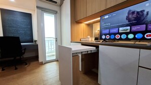 Et moderne kontorrum med et stort fladskærms-tv, der viser et streaming-tjeneste-interface, et skrivebord med stol og et vindue med persienner.