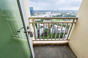 Een balkon met een metalen hekwerk, een groene deur en uitzicht op een stadslandschap met gebouwen en groen.