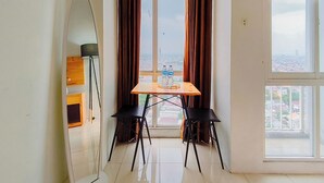 Ein Zimmer mit Tisch und zwei Stühlen, einem Fenster mit Vorhängen und Blick auf eine Stadtlandschaft.