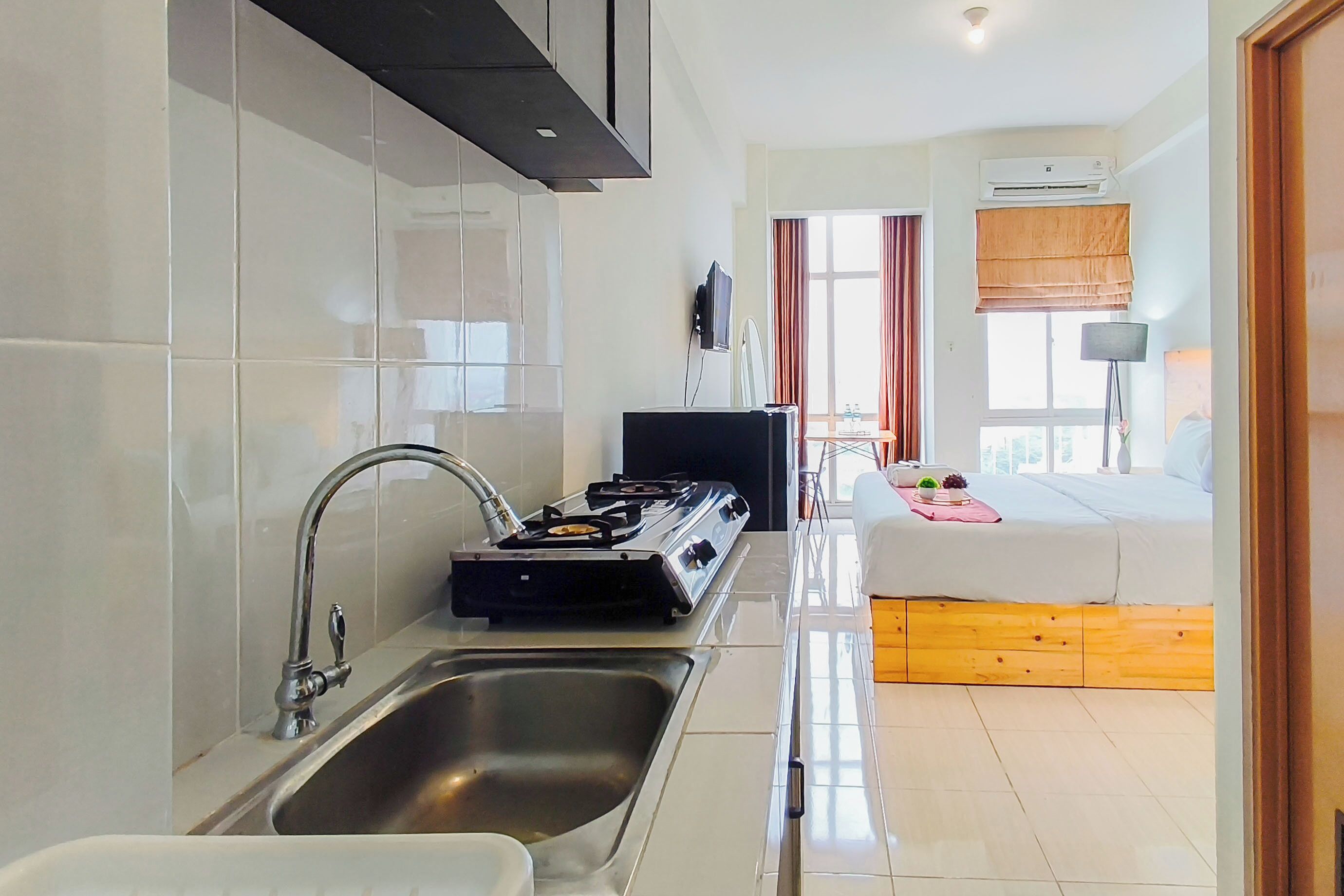 A modern kitchen with a gas stove, sink, and a flat-screen TV mounted on the wall.