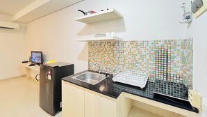 A kitchen with a black countertop, a stainless steel sink, a tiled backsplash, and a small shelf above the sink. - Studio Apartment Near Upn Veteran Yogyakarta At Barsa City (Depok)