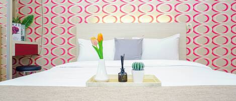A neatly made bed with a tray of toiletries, a potted plant, and a small cactus.