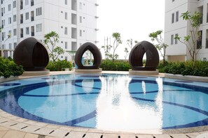 Une piscine avec trois grandes structures sphériques au centre, entourée de verdure et de bâtiments modernes en arrière-plan.