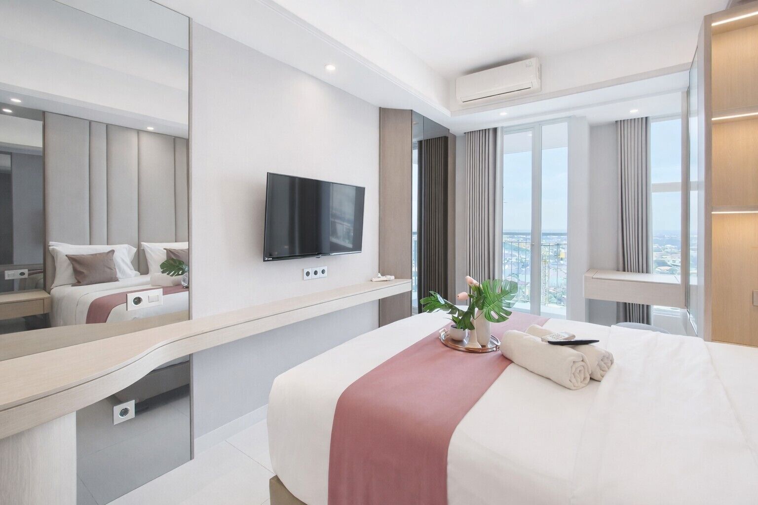 Ett modernt hotellrum med en stor säng, en platt-TV som är monterad på väggen, ett sängbord och ett stort fönster med utsikt över staden.