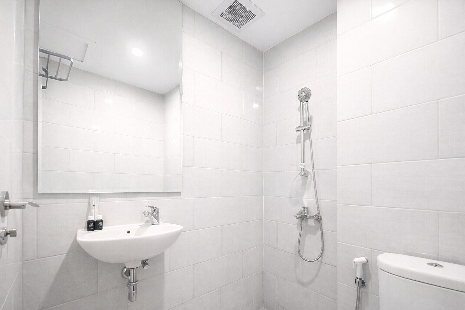 Een moderne badkamer met witte tegels, een wastafel, een spiegel en een douche.