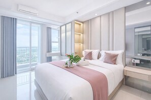 A modern hotel room with a large bed, a bedside table, a mirror, and a view of the city. - Magnificent Studio With Mall Access At Benson Supermall Mansion Apartment (Surabaya)