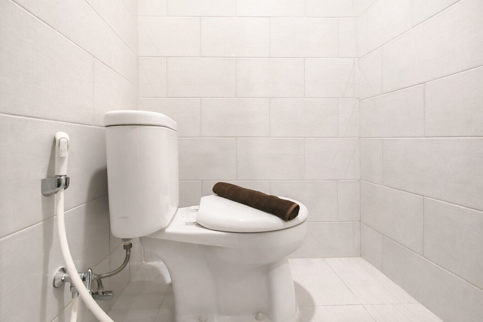 Eine weiße Toilette mit Handtuch auf dem Sitz, Spülhebel und einem Wasserschlauch.