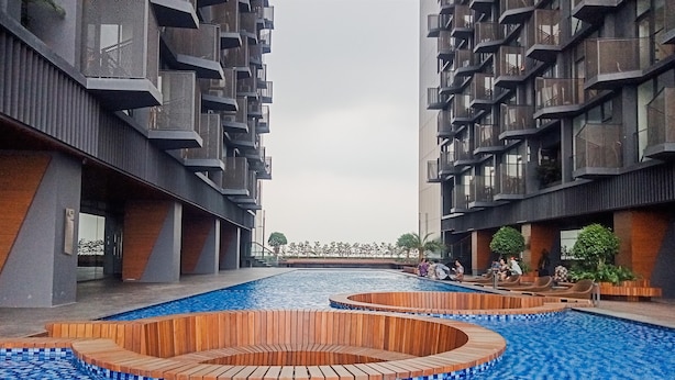 A modern building with a central pool area featuring wooden seating and a tiled floor. - Comfy And Nice Studio Apartment At Carstensz Residence (Gading Serpong)