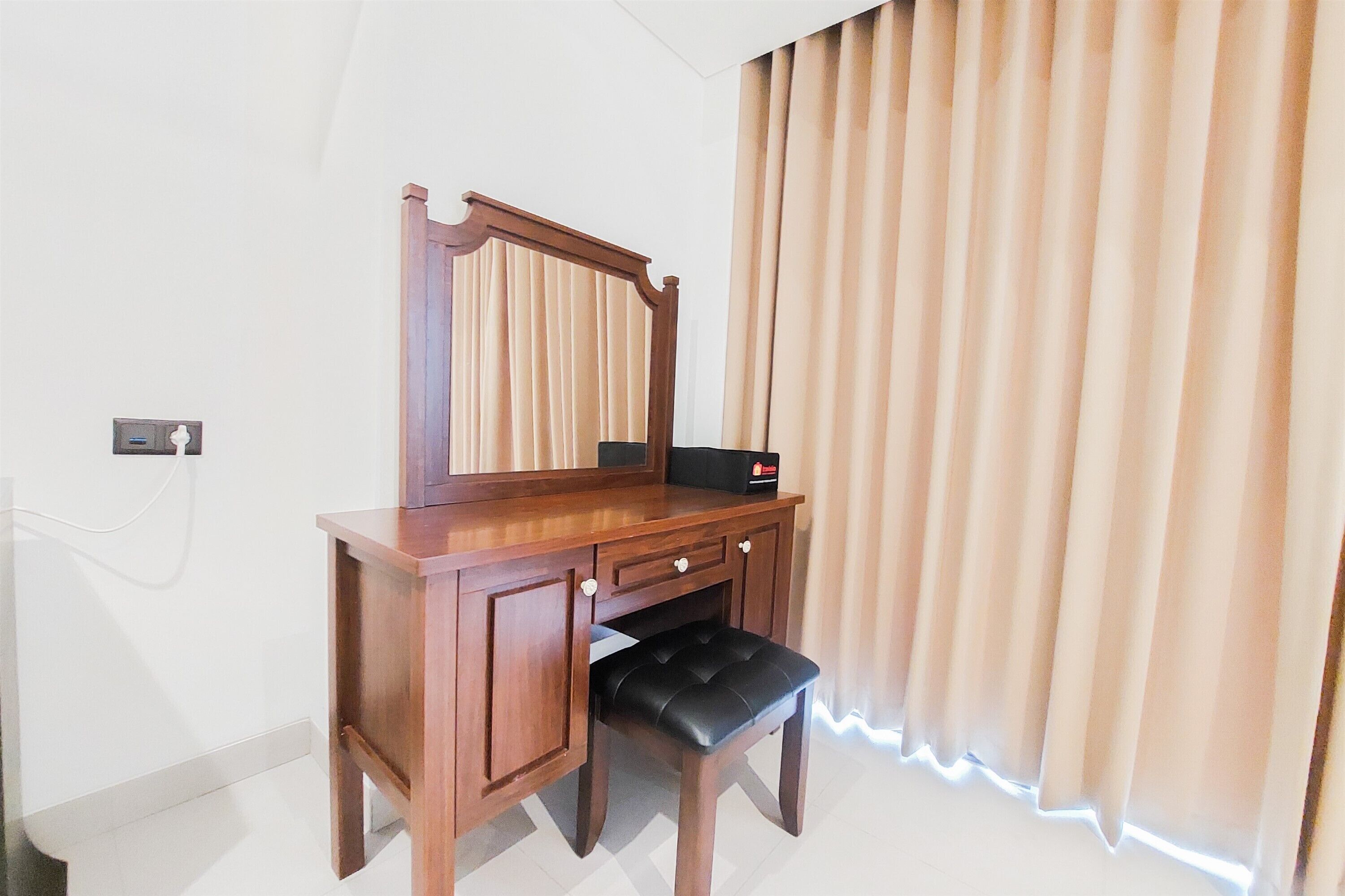 Un escritorio de madera con un espejo, un banco negro y una ventana con cortinas.
