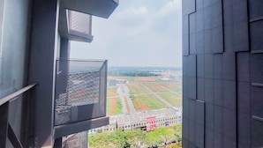 A view from a high-rise building with a clear sky, a road, and a building with a red sign in the distance. - Comfy And Nice Studio Apartment At Carstensz Residence (Gading Serpong)