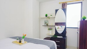 A bedroom with a bed, bedside table, dresser, mirror, shelves with plants, and a window. - Homey 2Br For 4 Pax At Cibubur Village Apartment (Depok)