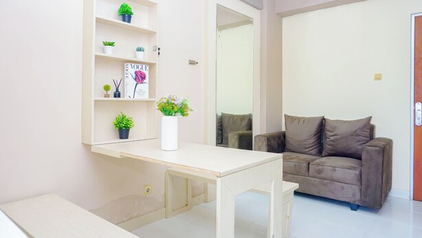 A living room with a sofa, a coffee table, a bookshelf with plants, and a magazine. - Homey 2Br For 4 Pax At Cibubur Village Apartment (Depok)