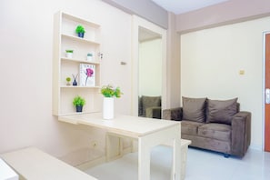A living room with a sofa, a coffee table, a bookshelf with plants, and a magazine. - Homey 2Br For 4 Pax At Cibubur Village Apartment (Depok)