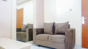 A room with a beige sofa, a white table, and a wooden door. - Homey 2Br For 4 Pax At Cibubur Village Apartment (Depok)