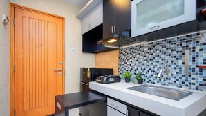 A compact kitchen with a wooden door, a microwave, a sink, and a tiled backsplash. - Comfortable Classic Studio At Apartment Cinere Bellevue Suites (Depok)