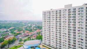 A high-rise building with multiple balconies, a swimming pool, and a view of a residential area. - Comfortable Classic Studio At Apartment Cinere Bellevue Suites (Depok)