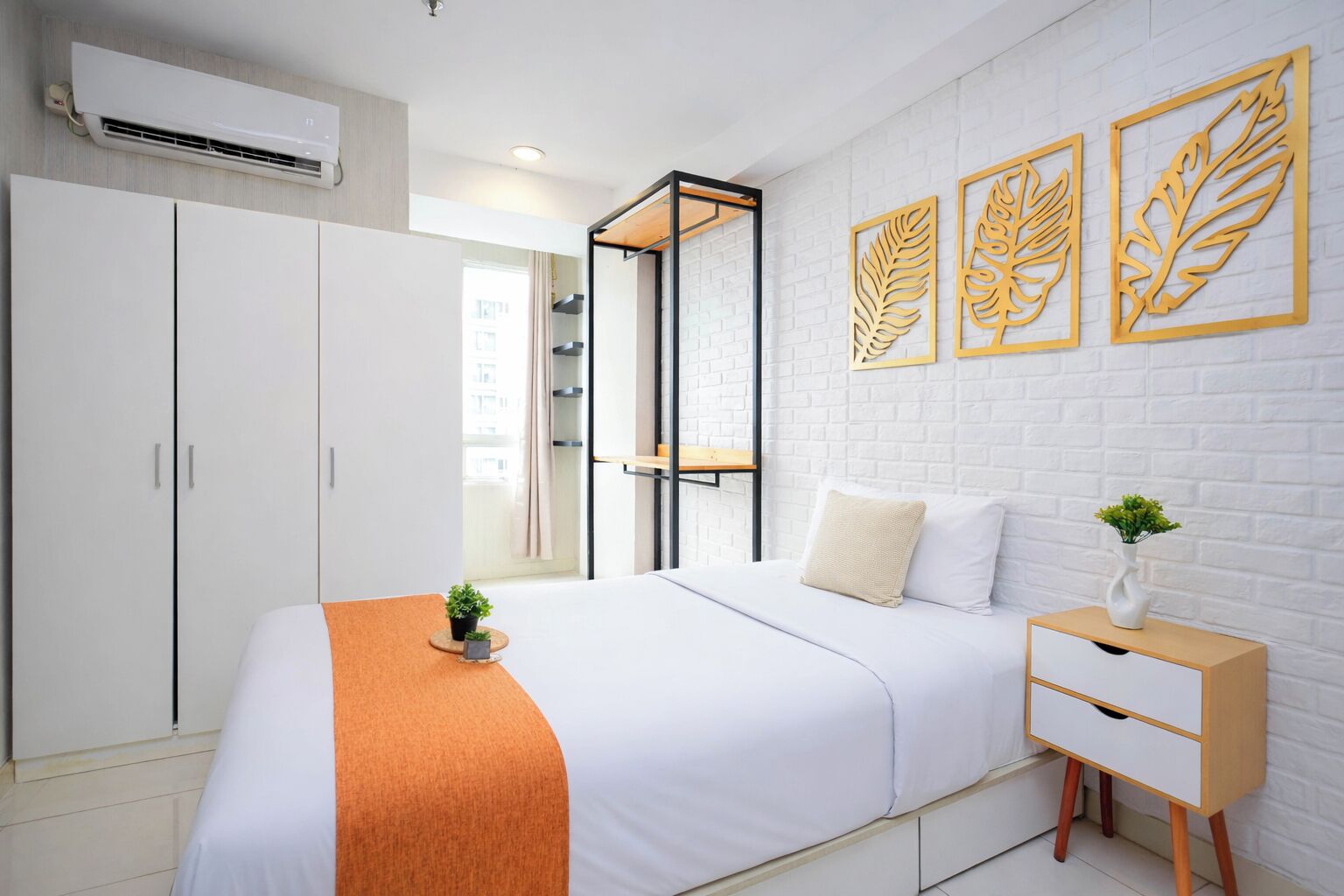 A bedroom with a bed, wardrobe, bedside table, and decorative leaf wall art.