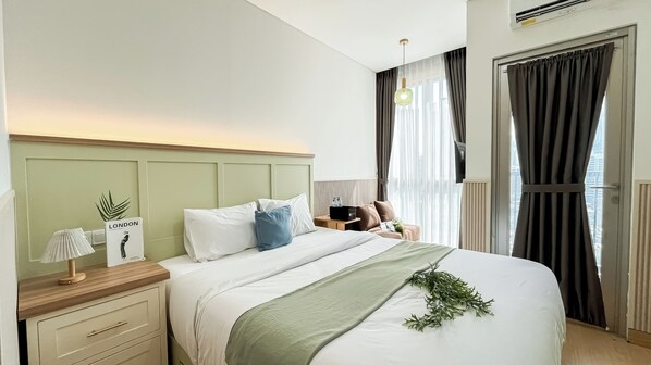 A hotel room with a bed, bedside table, lamp, and a view of the city through the window. - Urban Chic Studio Room At Ciputra World 2 Apartment (Jakarta)