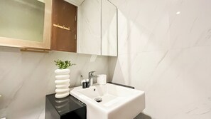 A bathroom with a white sink, a mirror, a towel, and a plant. - Urban Chic Studio Room At Ciputra World 2 Apartment (Jakarta)
