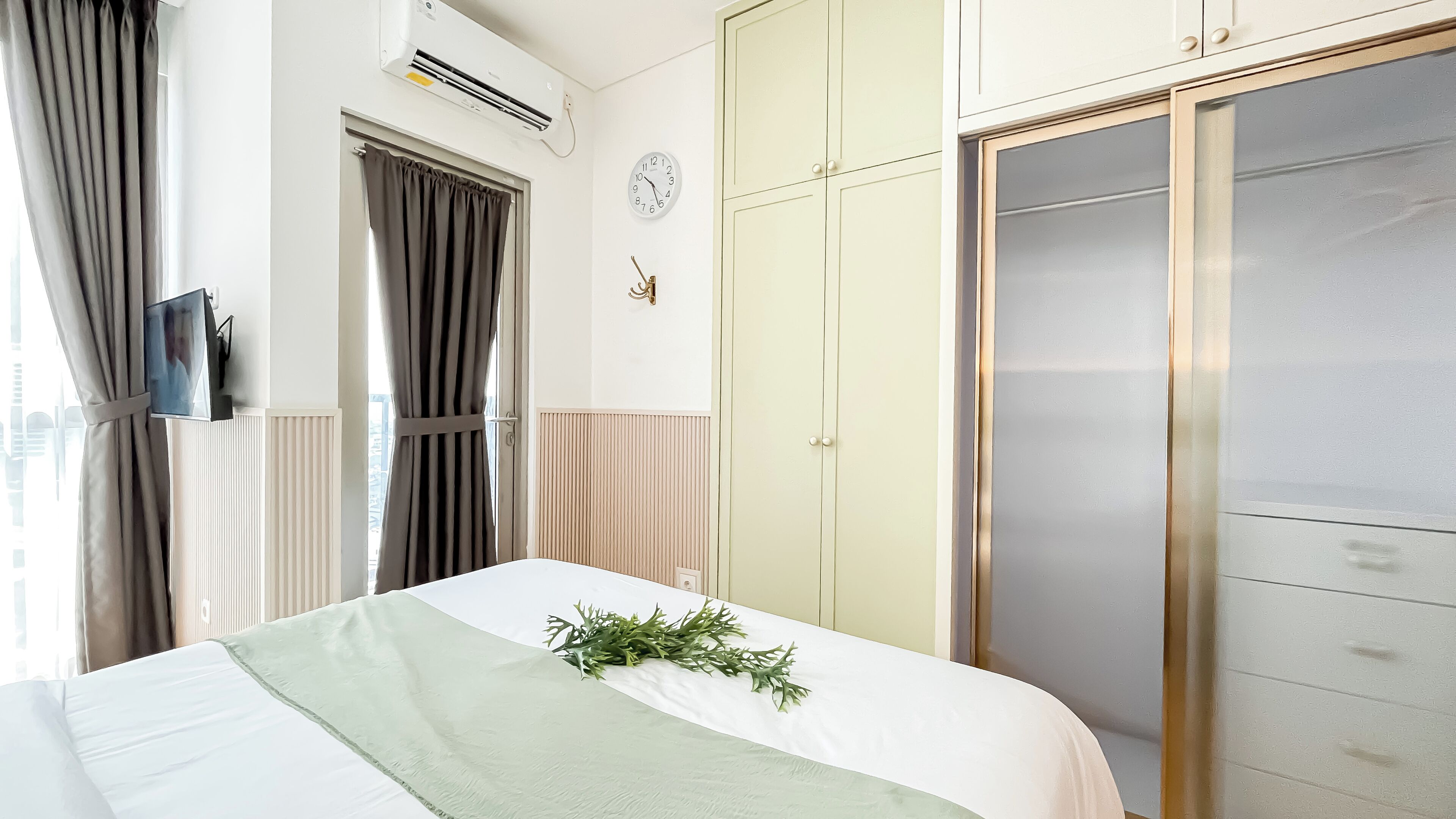 Hotellihuone, jossa on sänky, vaatekaappi, kello ja ilmastointilaite.